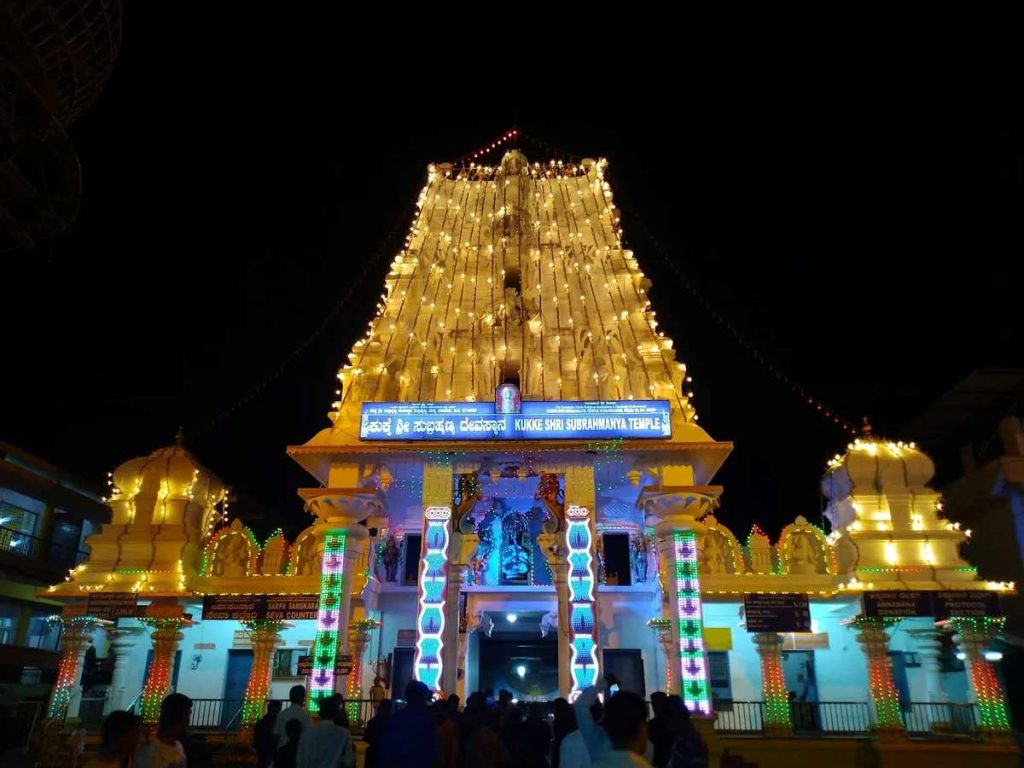 Kukke Subramanya Temple illuminated at night with decorative lights and devotees at entrance