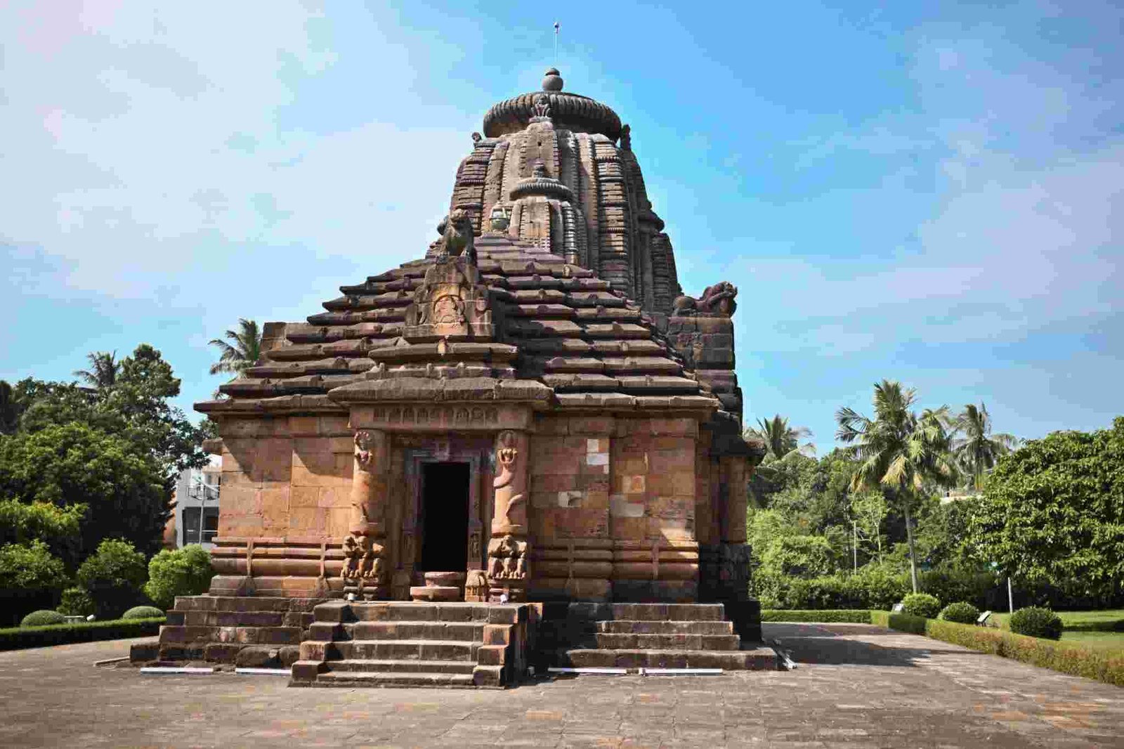 Ancient Rajarani Temple in Bhubaneswar featuring traditional Kalinga-style architecture surrounded by greenery and a clear blue sky.